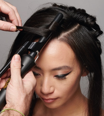 modèle féminin plan de dessus, on aperçoit le fer à boucler qui enroule une mèche de checeu près du cuir chevelu