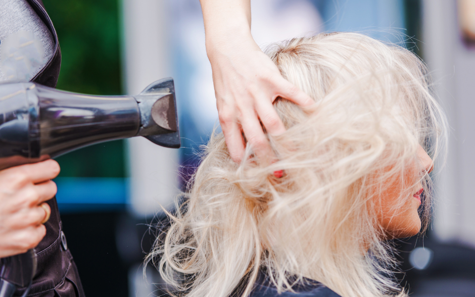 Séchage des cheveux au doigts. La chevelure blonde secouée entre les doigts de la coiffeuse pour laisser passer l'air du sèche cheveu